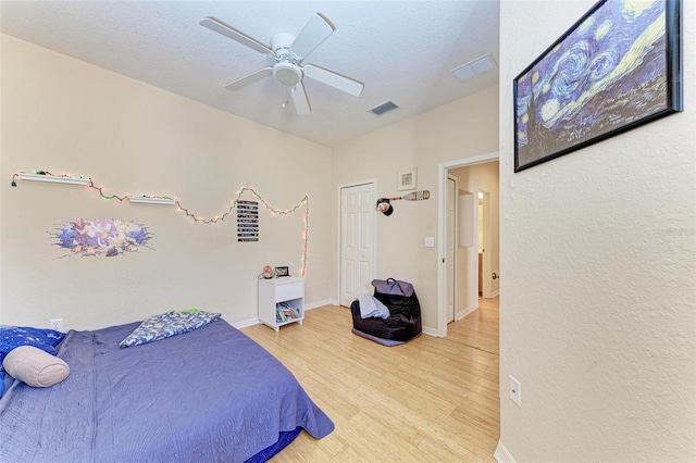 bedroom with light hardwood / wood-style floors, ceiling fan, and a textured ceiling