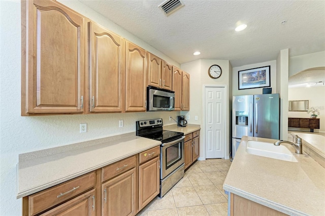 kitchen featuring appliances with stainless steel finishes, light tile patterned floors, sink, and a textured ceiling