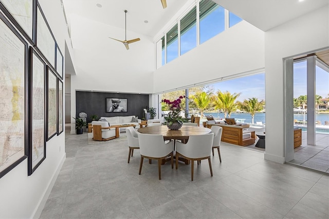 dining area with a towering ceiling, a water view, and ceiling fan