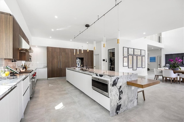 kitchen with white cabinets, stainless steel appliances, hanging light fixtures, and exhaust hood