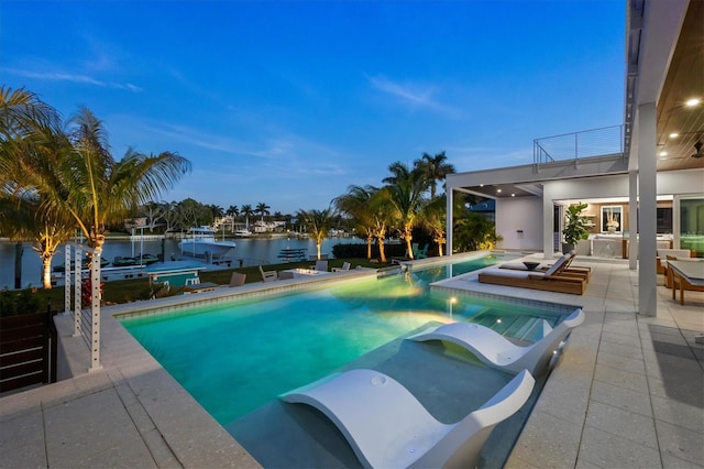 pool at dusk featuring a patio and a water view