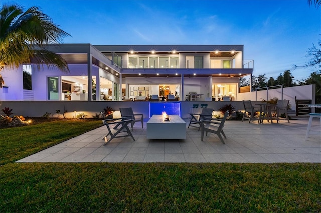 back house at dusk featuring a yard, a balcony, a patio, and an outdoor fire pit