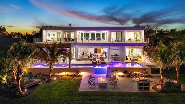 back house at dusk featuring an outdoor living space, a balcony, a yard, and a patio