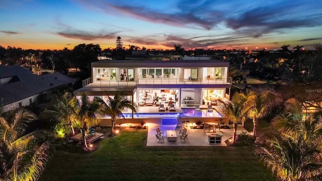 back house at dusk with a lawn, an outdoor hangout area, a balcony, a bar, and a patio