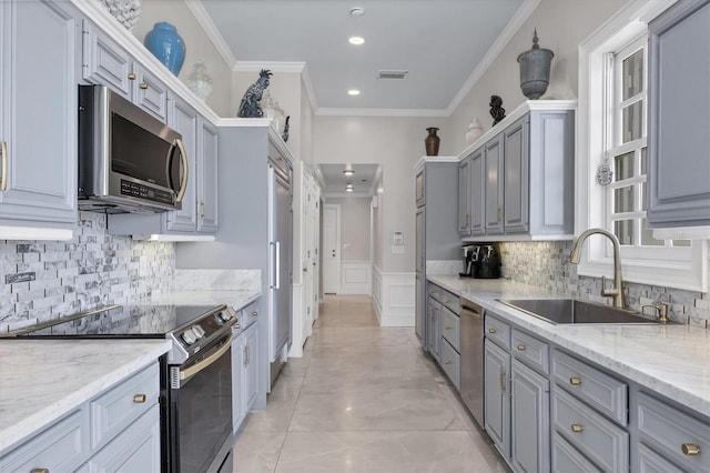 kitchen featuring appliances with stainless steel finishes, gray cabinetry, ornamental molding, light stone counters, and sink