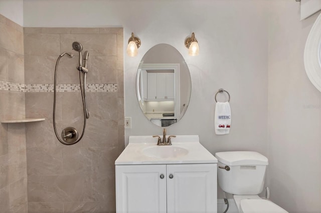 bathroom with toilet, a tile shower, and vanity