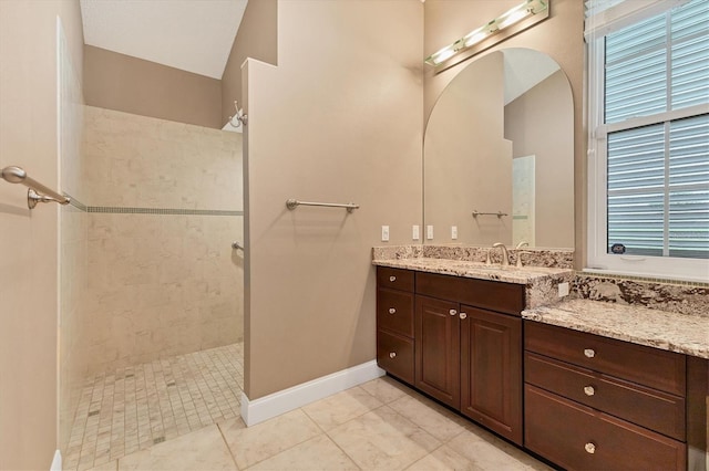 bathroom featuring a tile shower, vanity, tile patterned floors, and vaulted ceiling