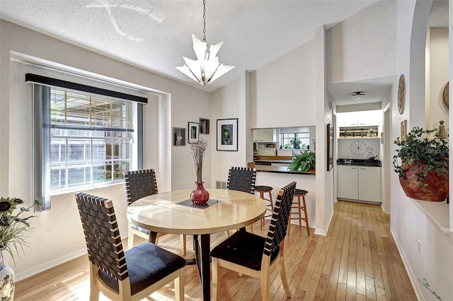 dining room featuring a textured ceiling, light wood-type flooring, high vaulted ceiling, and a notable chandelier