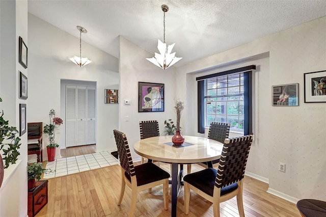 dining room with hardwood / wood-style floors, a textured ceiling, a chandelier, and high vaulted ceiling