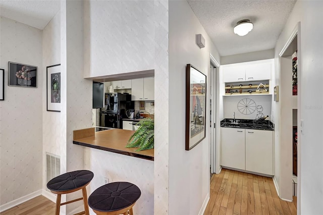 corridor featuring sink, a textured ceiling, and light hardwood / wood-style flooring