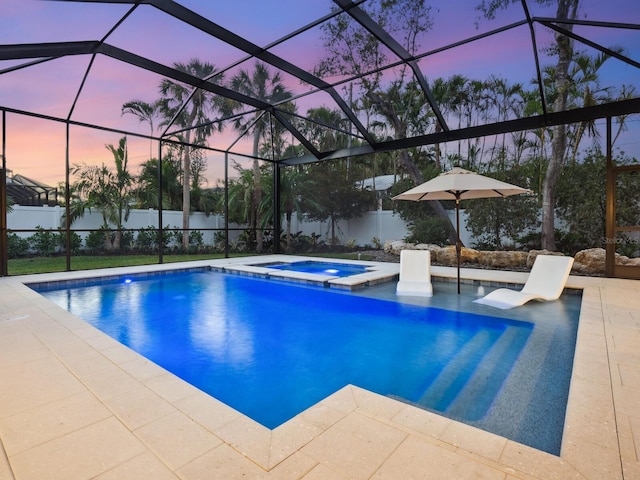 pool at dusk with glass enclosure, an in ground hot tub, and a patio area