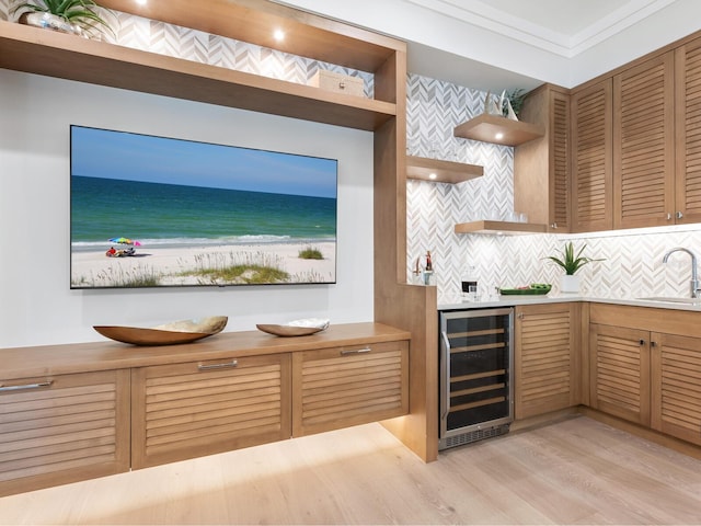 bar with backsplash, sink, crown molding, light wood-type flooring, and beverage cooler