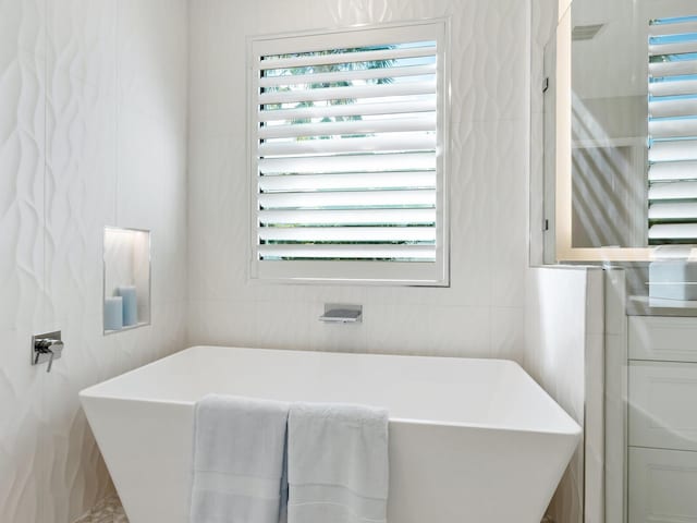 bathroom featuring a tub to relax in and tile walls