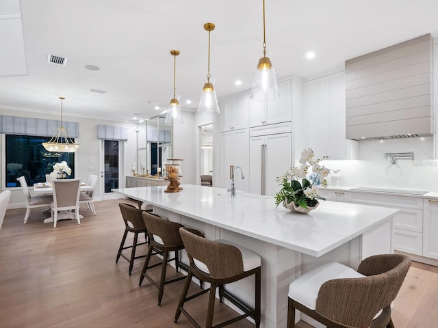 kitchen featuring a kitchen breakfast bar, a large island with sink, decorative light fixtures, and paneled refrigerator