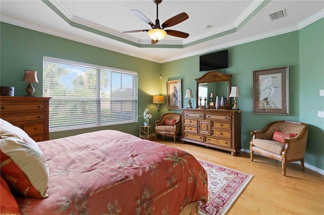 bedroom featuring light wood-type flooring, a raised ceiling, ceiling fan, and ornamental molding