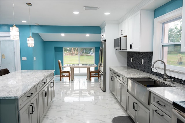 kitchen with stainless steel appliances, a wealth of natural light, light stone countertops, and decorative backsplash