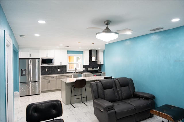 kitchen with appliances with stainless steel finishes, hanging light fixtures, wall chimney exhaust hood, and white cabinets