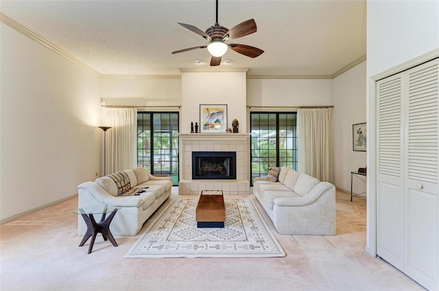 living room with ornamental molding, a textured ceiling, light carpet, a tiled fireplace, and ceiling fan