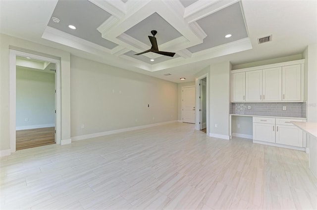 unfurnished living room featuring coffered ceiling, ornamental molding, ceiling fan, a raised ceiling, and light hardwood / wood-style flooring