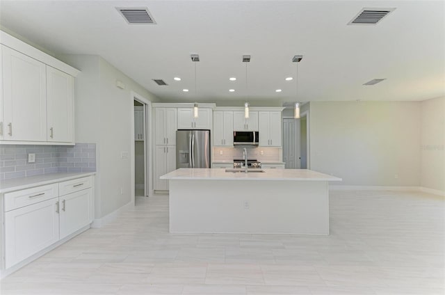 kitchen with tasteful backsplash, appliances with stainless steel finishes, hanging light fixtures, an island with sink, and white cabinets