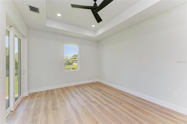 empty room with ceiling fan, a raised ceiling, and light hardwood / wood-style flooring