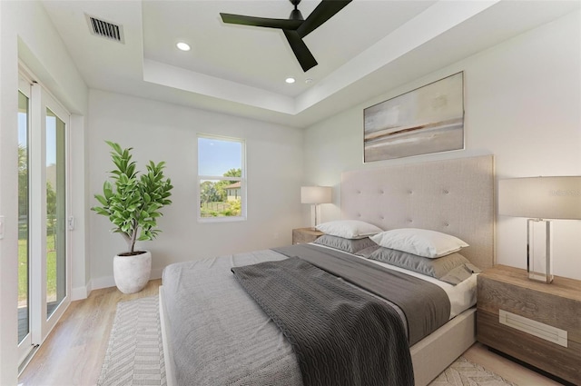 bedroom featuring access to exterior, light hardwood / wood-style floors, ceiling fan, and a raised ceiling