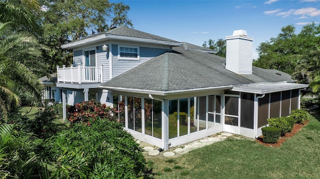 back of property with a sunroom, a balcony, and a lawn