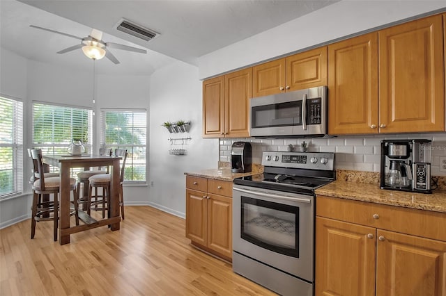 kitchen with appliances with stainless steel finishes, light stone countertops, light hardwood / wood-style flooring, and backsplash