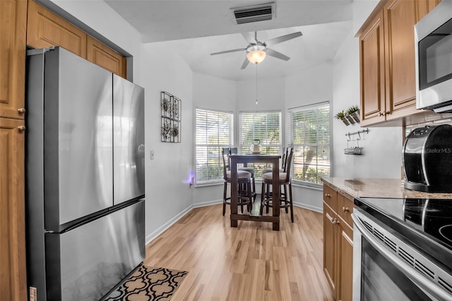 kitchen with ceiling fan, appliances with stainless steel finishes, light stone counters, and light hardwood / wood-style floors