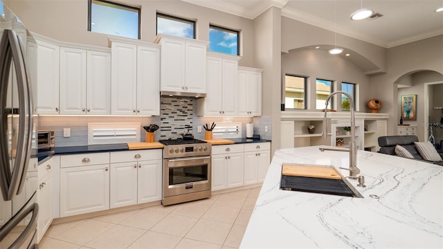 kitchen featuring white cabinets, ornamental molding, appliances with stainless steel finishes, and dark stone counters