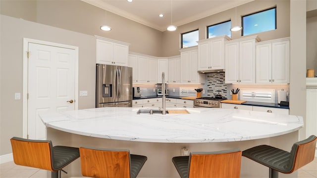 kitchen featuring a breakfast bar, stainless steel appliances, light tile patterned floors, decorative light fixtures, and white cabinetry