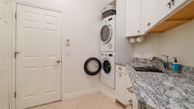 laundry area featuring sink, light tile patterned floors, cabinets, and stacked washer / drying machine