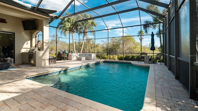 view of pool featuring glass enclosure, outdoor lounge area, an outdoor kitchen, a grill, and a patio