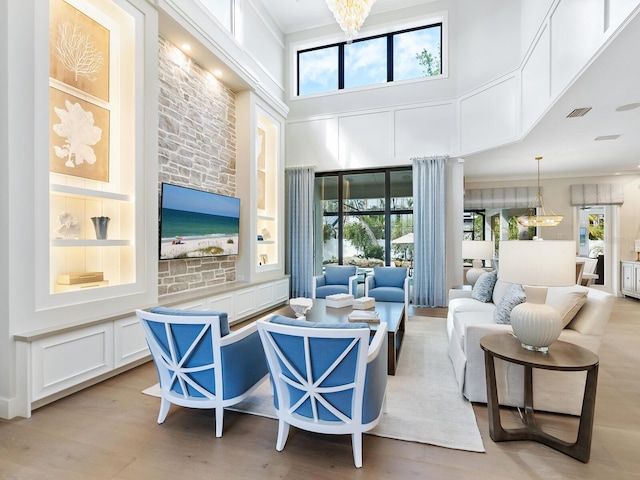 living room featuring light wood-type flooring, a towering ceiling, an inviting chandelier, and built in features