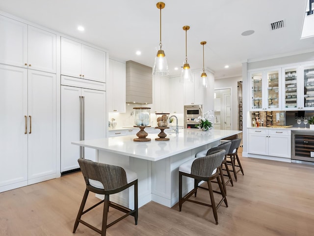 kitchen featuring paneled built in fridge, an island with sink, white cabinetry, a breakfast bar area, and beverage cooler