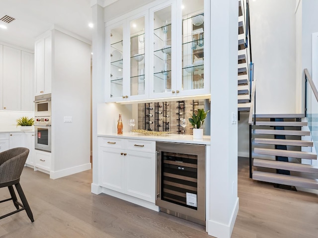 bar featuring white cabinets, stainless steel double oven, light hardwood / wood-style flooring, and wine cooler