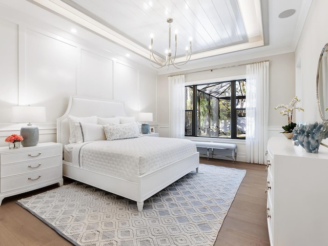 bedroom featuring a chandelier, wood-type flooring, ornamental molding, and a tray ceiling