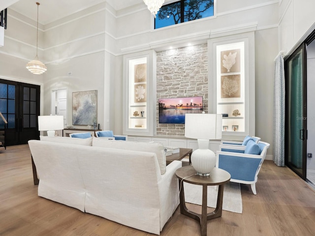 living room featuring french doors, light wood-type flooring, built in shelves, a chandelier, and a high ceiling