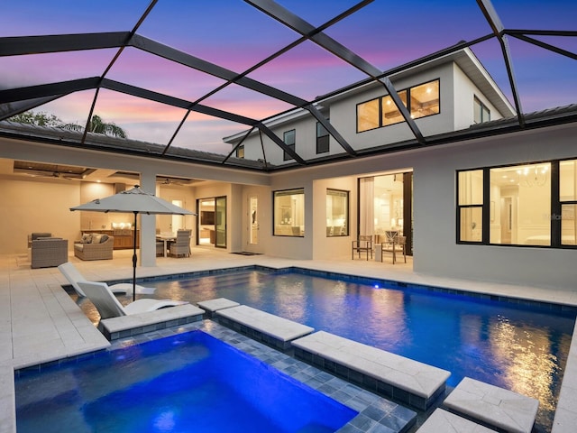 pool at dusk with glass enclosure, a patio area, an outdoor hangout area, and an in ground hot tub