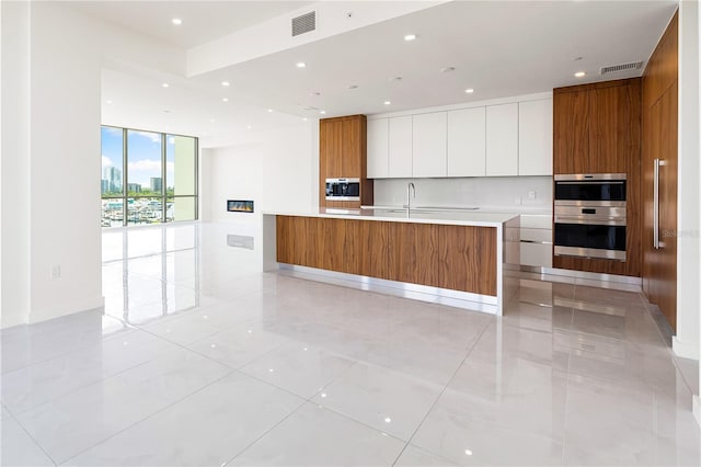 kitchen with sink, multiple ovens, light tile patterned floors, a wall of windows, and white cabinets