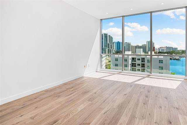 unfurnished room with a water view, floor to ceiling windows, plenty of natural light, and light hardwood / wood-style flooring