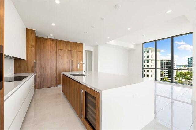 kitchen with a large island, sink, a wall of windows, beverage cooler, and white cabinets