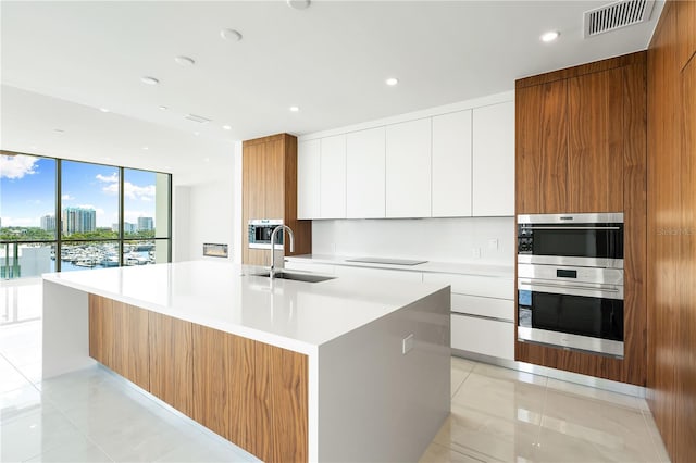 kitchen featuring light tile patterned flooring, white cabinetry, sink, a large island with sink, and floor to ceiling windows