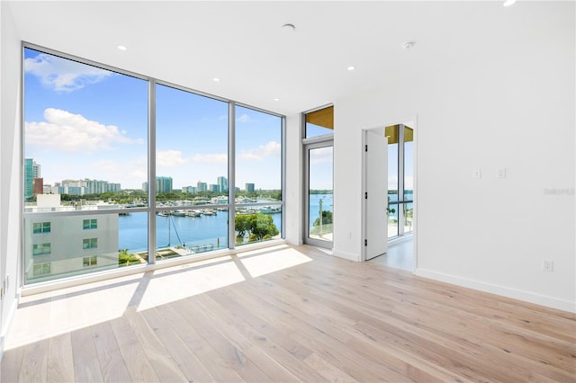 unfurnished room with light hardwood / wood-style flooring, floor to ceiling windows, and a water view