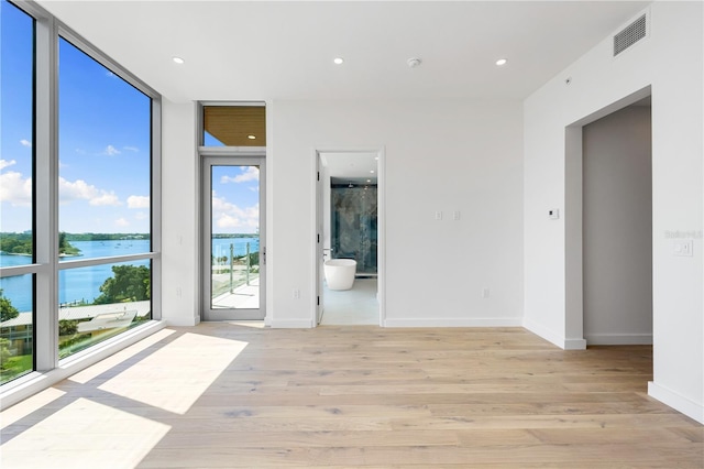 spare room with a water view, plenty of natural light, expansive windows, and light wood-type flooring