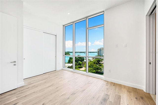 unfurnished bedroom featuring a water view, a wall of windows, light hardwood / wood-style floors, and a closet