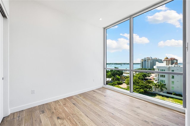 unfurnished room with a water view, a wall of windows, and light wood-type flooring