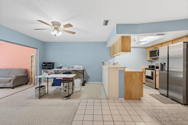 kitchen featuring a textured ceiling, light tile patterned floors, ceiling fan, a skylight, and appliances with stainless steel finishes