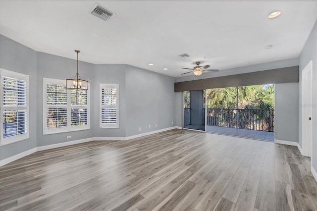 unfurnished living room featuring ceiling fan with notable chandelier and light wood-type flooring