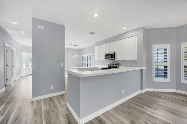 kitchen featuring pendant lighting, kitchen peninsula, light hardwood / wood-style flooring, appliances with stainless steel finishes, and white cabinetry